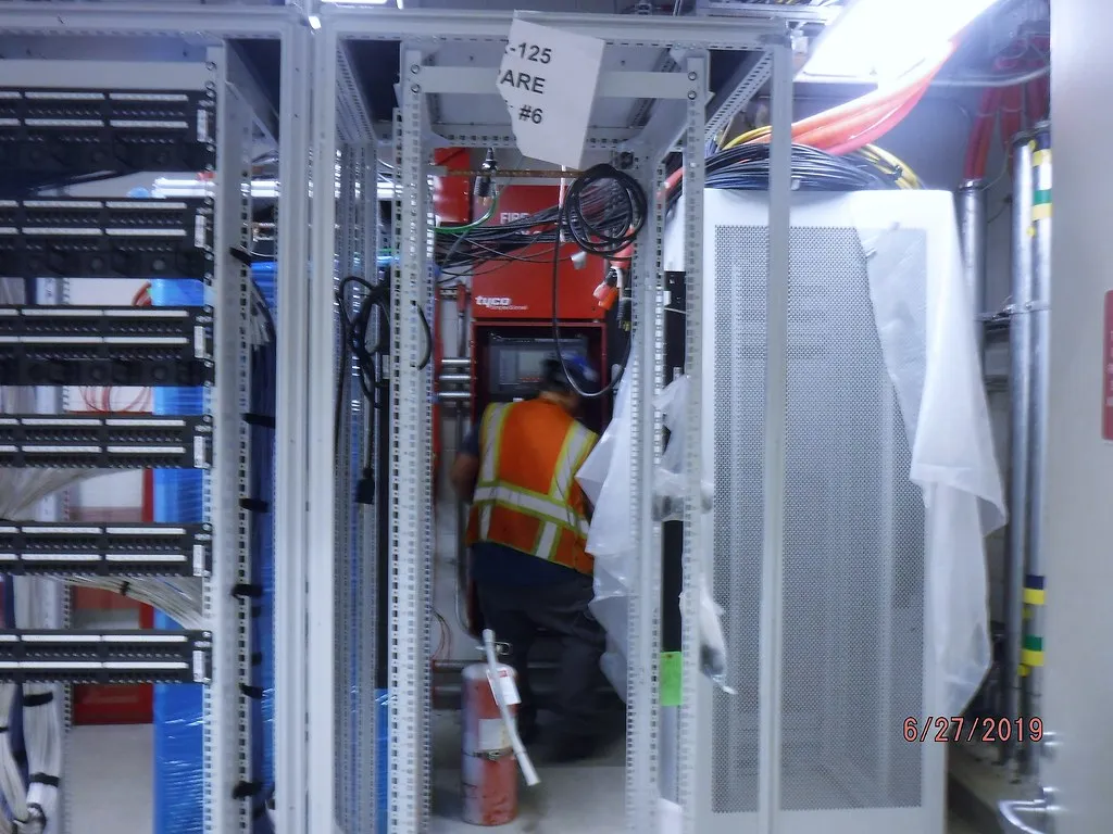 Técnico con chaleco reflectivo revisando un panel de control de incendio entre racks de equipos